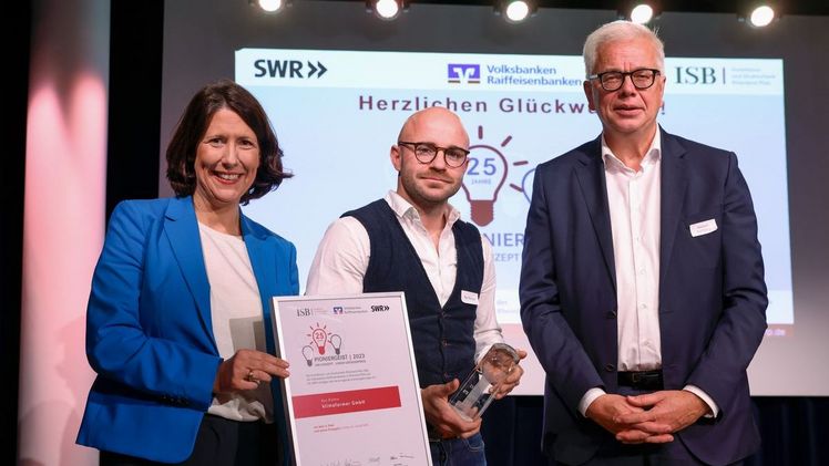 Ron Richter von der klimafarmer GmbH (mi.) bekommt den Preis "Pioniergeist 2023" von der rheinland-pfälzischen Wirtschaftsministerin Daniela Schmitt (li.) und Herbert Kohlberg, Vorstandsmitglied der Volksbank Darmstadt Mainz eG, überreicht. Foto: ISB/Alexander Sell.